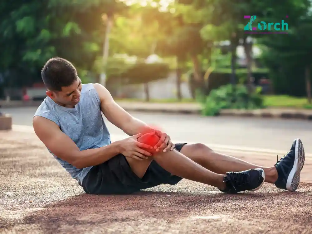 Young athlete sitting on road holding his knee in pain – illustrating common reasons of knee pain in young age including sports injury, overuse, and poor posture.